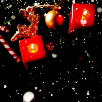 Snow falling against two christmas red square candles