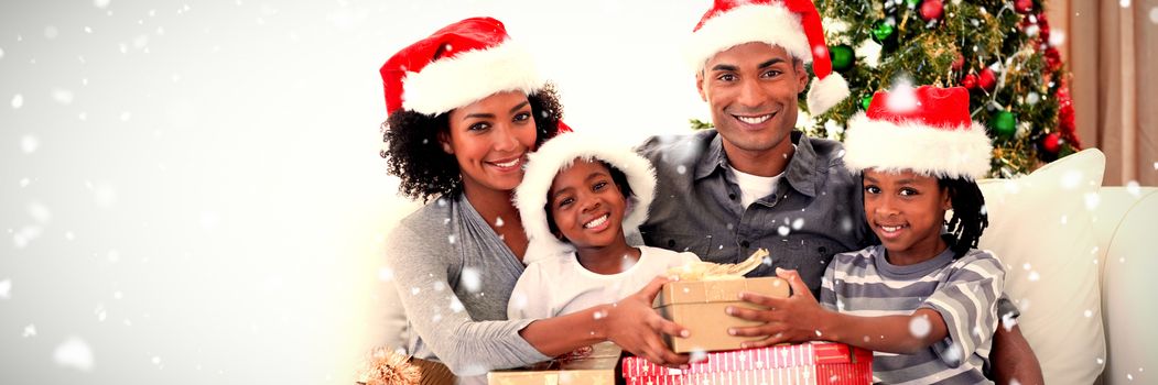 Smiling family sharing Christmas presents against snow falling