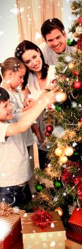 Happy family decorating a Christmas tree with boubles against snow falling