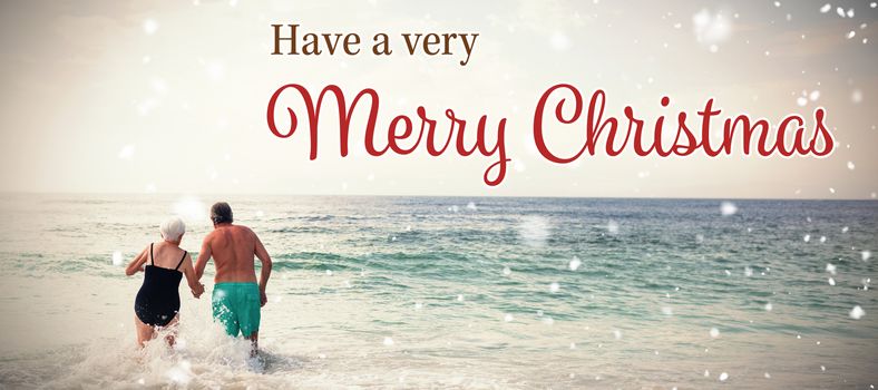 Christmas card against rear view of senior couple holding hands and walking in sea