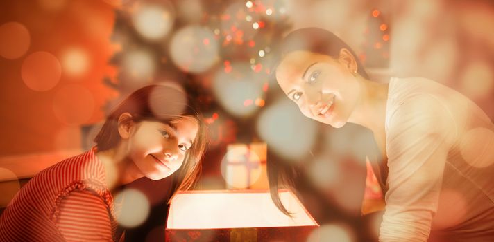 Festive mother and daughter opening a glowing christmas gift against light circles on black background