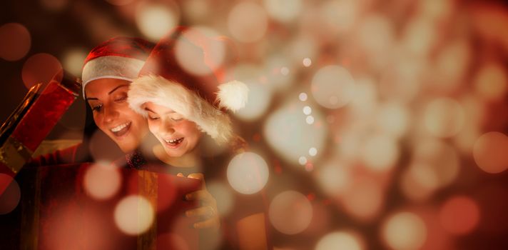 Festive mother and daughter opening a christmas gift against light circles on black background