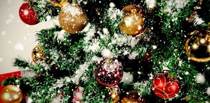 Snow falling against christmas balls in tree covered in snow