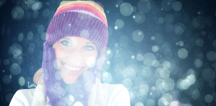 Radiant young woman with cap and gloves in the winter against blue abstract light spot design