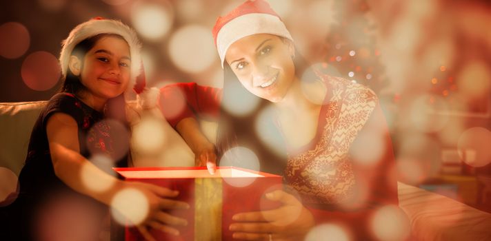 Festive mother and daughter opening a glowing christmas gift against light circles on black background