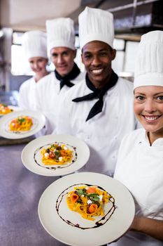 Group of chefs holding plate of pastas in kitchen at hotel