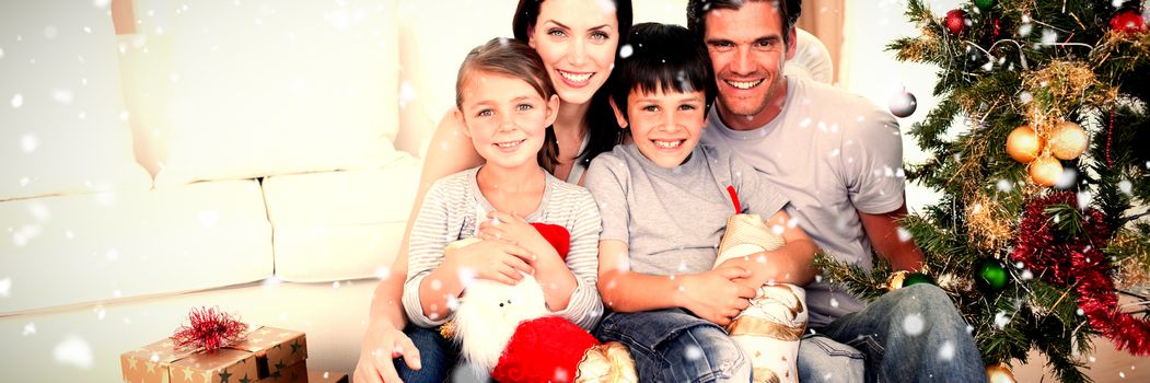 Happy family at Christmas time holding lots of presents against snow falling