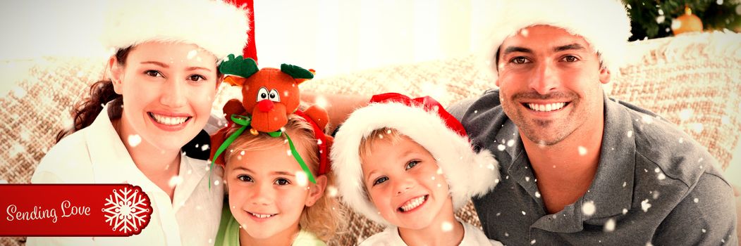 Portrait of a happy family with Christmas hats sitting on the sofa against banner sending love