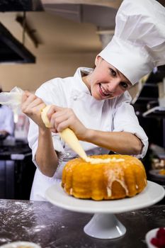 Female chef piping a cake in kitchen at hotel