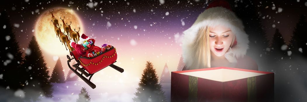Festive blonde looking into glowing gift against full moon over snowy landscape and house