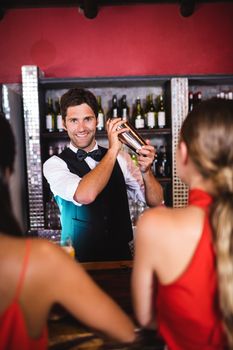 Bartender shaking cocktail in cocktail shaker at bar counter in nightclub
