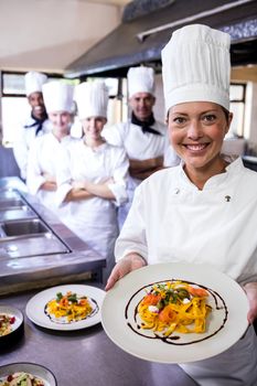 Group of chefs holding plate of prepared pasta in kitchen at hotel