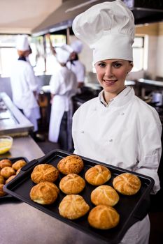 Female chefs holding baking tray of kaiser rolls in kitchen at hotel