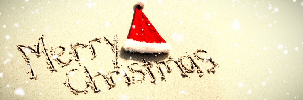 Snow falling against merry christmas written on sand with santa hat