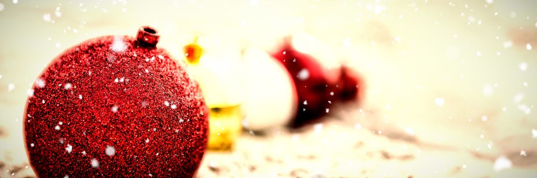 Snow falling against christmas colorful baubles arranged on sand