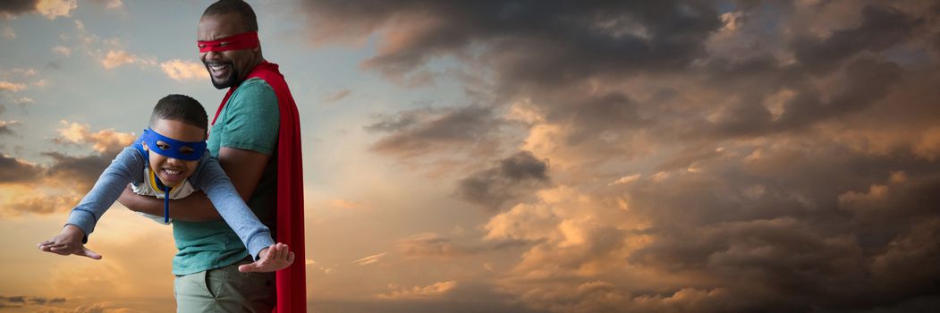 Father and son pretending to be superhero against blue and orange sky with clouds