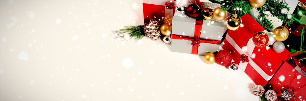 Snow falling against christmas gift and pine cone under the tree