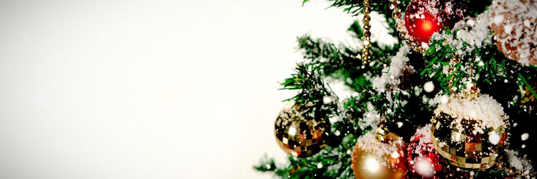 Snow falling against christmas ornaments hanging in tree