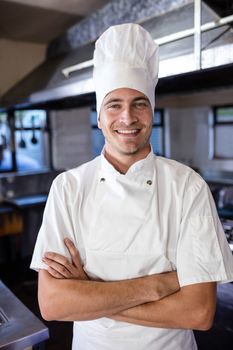 Male chef standing with arms crossed in kitchen at hotel