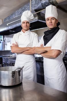 Two male chefs standing with arms crossed in kitchen at hotel