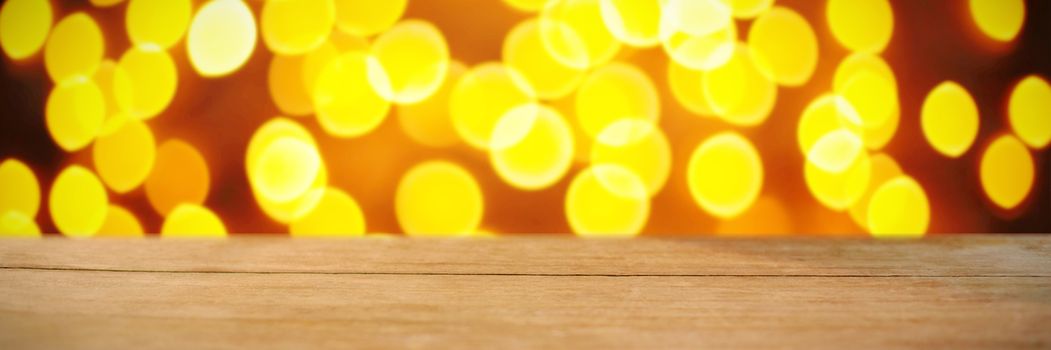 Composite image of wooden table against unfocused yellow christmas light