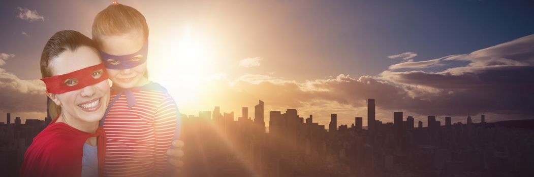 Mother and daughter pretending to be superhero against picture of city by sunrise