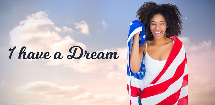 Pretty girl wrapped in american flag smiling at camera against colored sky with clouds