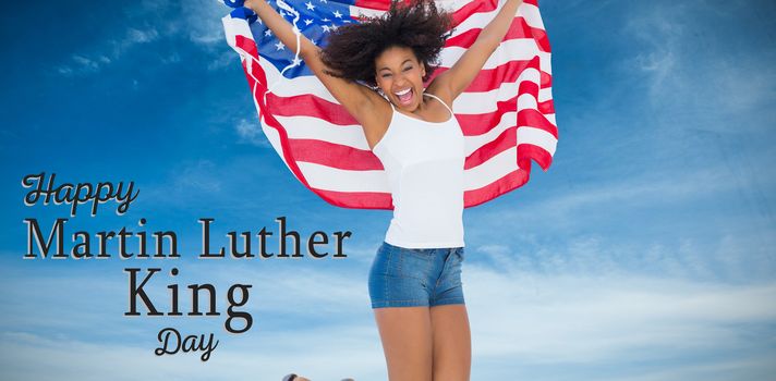 Pretty girl wrapped in american flag jumping and smiling at camera against low angle of cloudy sky 