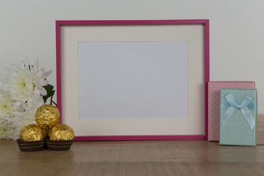 Chocolates, flowers, empty photo frame and gift boxes on wooden table