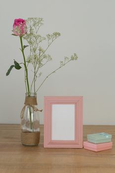 Rose flower, empty photo frame and gift boxes on wooden table
