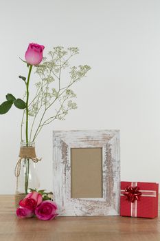 Rose flower, empty photo frame and gift boxes on wooden table