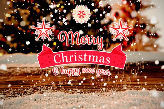 Christmas card against wooden table with snow and unfocused christmas tree