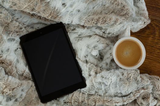 Close-up of digital tablet with blanket and coffee on wooden background