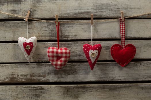 Heart shape decorations hanging on thread against wooden plank
