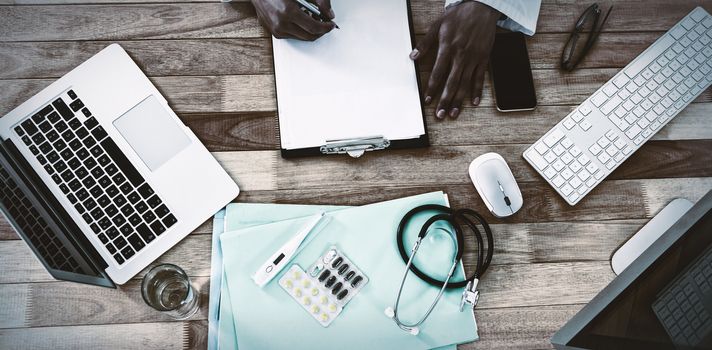 Cropped hand of doctor writing on clipboard at desk