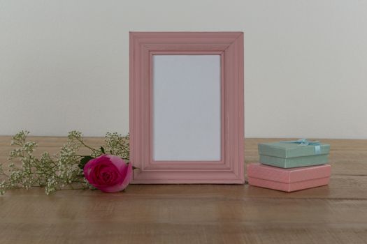 Rose flower, empty photo frame and gift boxes on wooden table