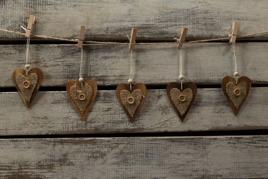 Heart shape decorations hanging on thread against wooden plank