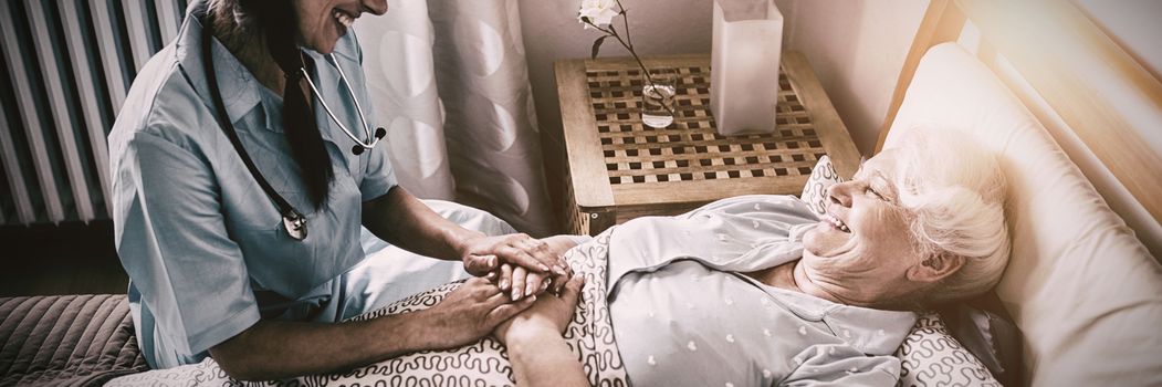 Nurse interacting with senior woman on bed at bedroom