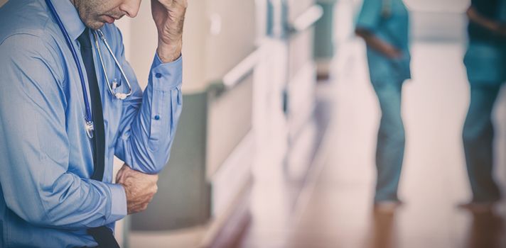 Sad doctor against the wall in hospital corridor