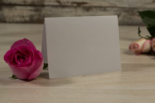 Close-up of card and rose flowers on wooden table