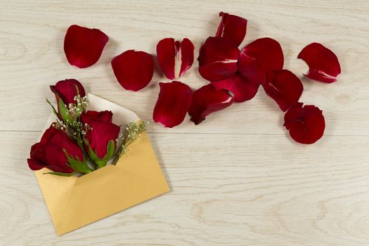 Rose bouquet and petals with envelope on wooden table