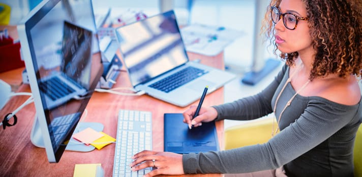 Female graphic designer working on computer while using graphic tablet at desk in the office