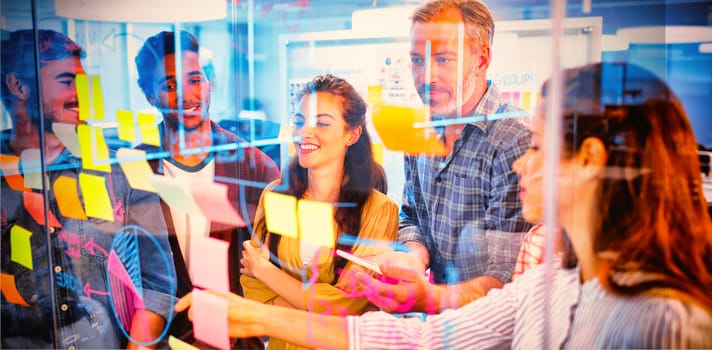 Creative business team looking at sticky notes on glass window in office