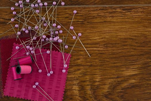 Thread rolls, sewing pins and textile on wooden table