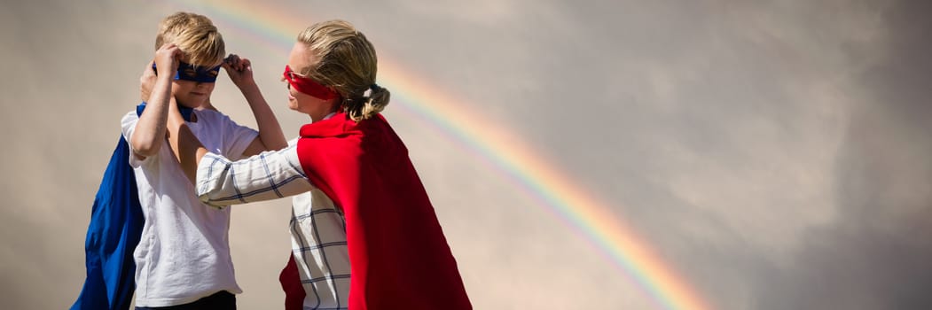 Mother and son pretending to be superhero against rainbow in a dark sky above the green hill