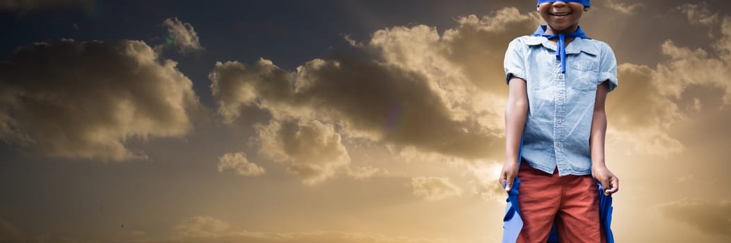 Boy pretending to be superhero against cloudy sky landscape