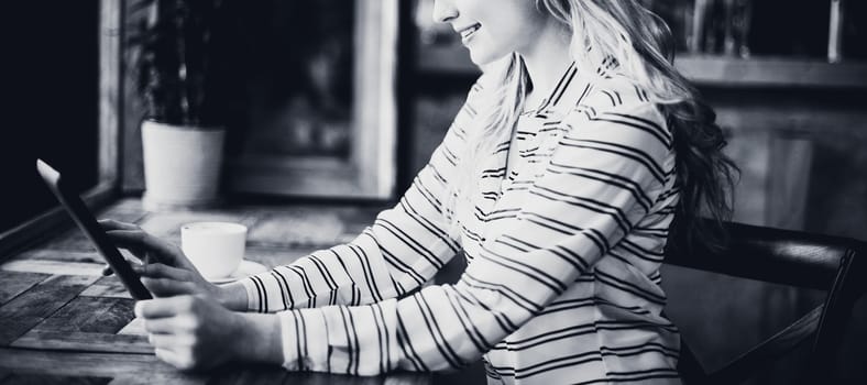 Smiling woman using digital tablet while having coffee in cafÃ©