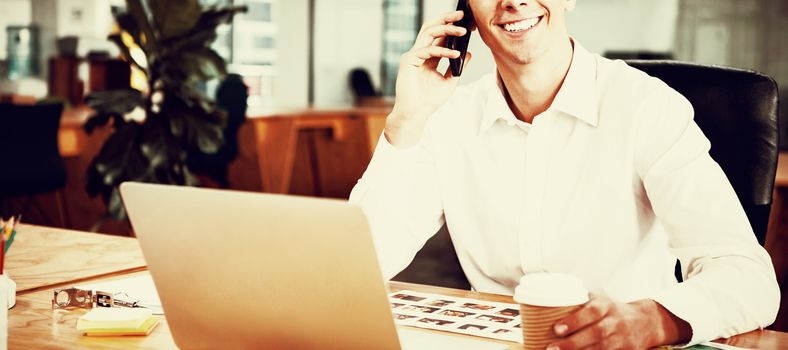 Happy man talking on mobile phone at desk in creative office