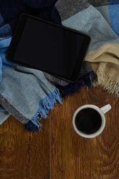 Close-up of digital tablet with blanket and black coffee on wooden background