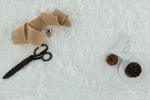 Overhead of textile, scissors and pine cone on white background